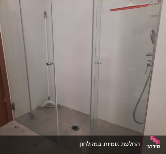 מקלחון זכוכית שקוף מותקן בחדר רחצה עם דלתות ציר